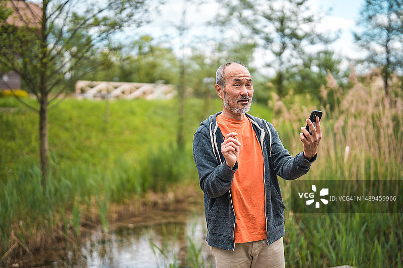 在公园里进行视频通话的快乐中年亚洲男人图片素材