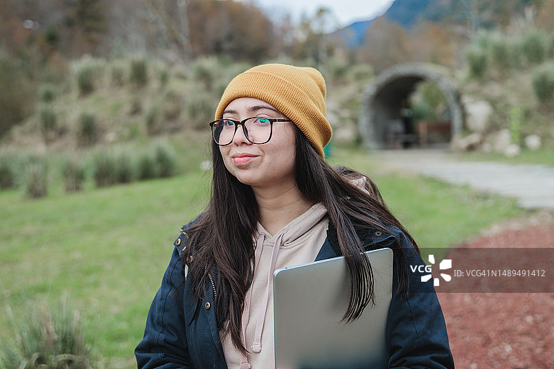 年轻的数字游民女性穿着保暖的衣服，带着笔记本电脑在迷人的乡村风景中开始宁静的旅程图片素材