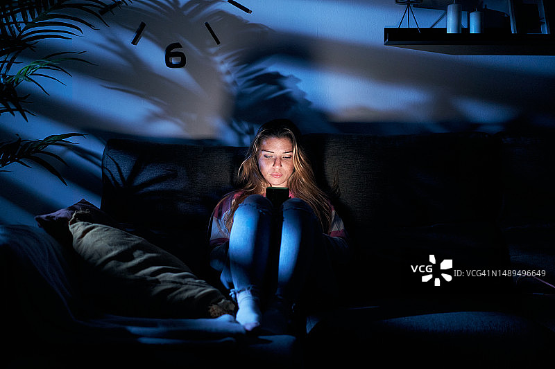 金发女人客厅月光下玩智能手机图片素材