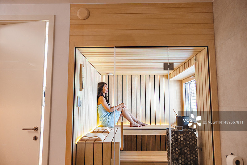 Привлекательная белая женщина в полотенце расслабляется в домашней сауне после долгого дня图片素材