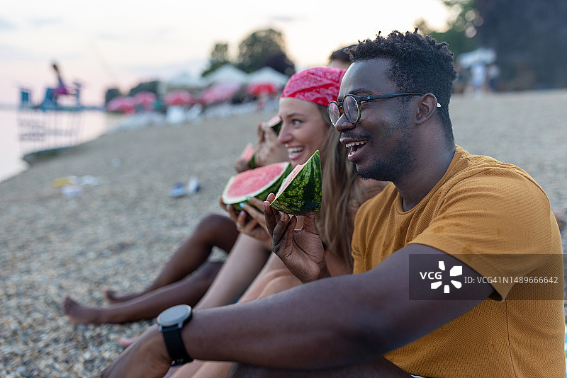 一位年轻的非洲男子和他的女性朋友在河岸边，附近有西瓜。图片素材