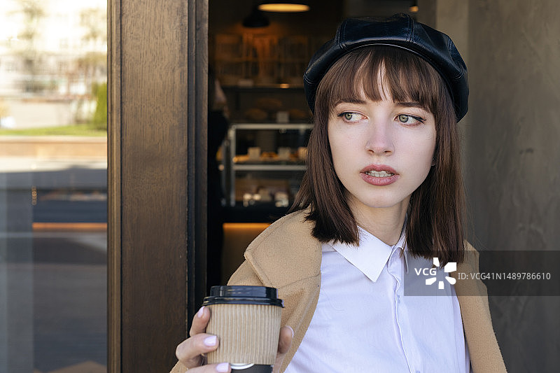 戴贝雷帽穿米色外套的年轻女人走出咖啡店图片素材