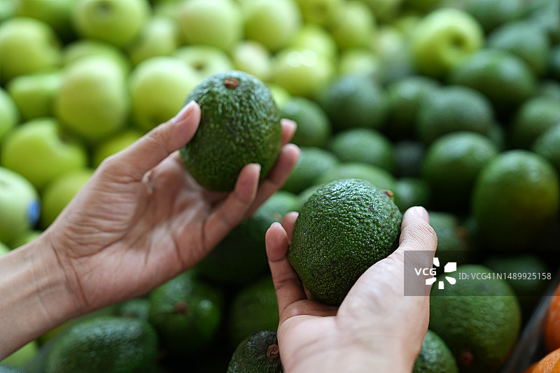 年轻的亚洲女性在农产品通道购买新鲜鳄梨。日常购物，健康饮食图片素材