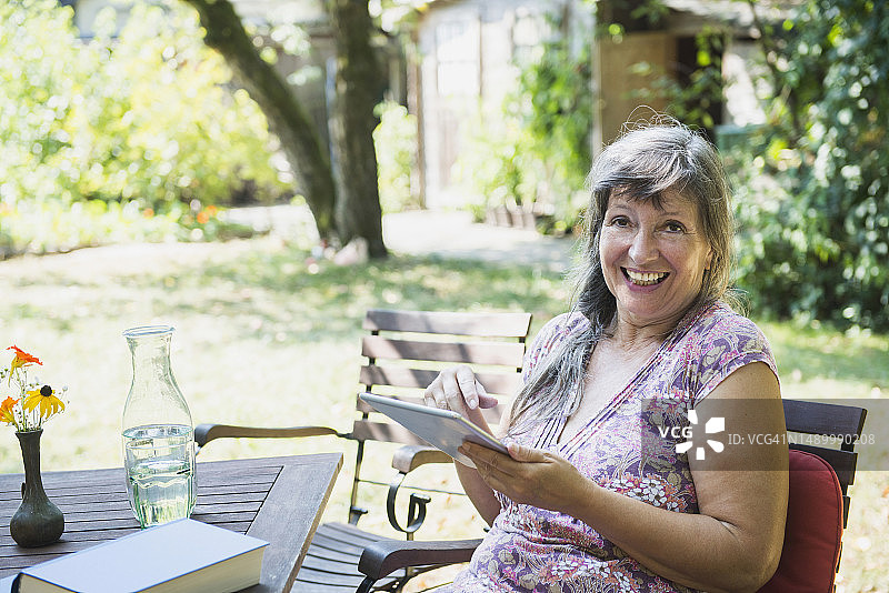 手持平板电脑的年长女性在德国巴伐利亚州阿尔特廷的花园里图片素材