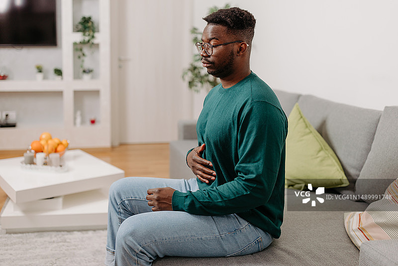 非裔美国男子在客厅沙发上感到胃痛图片素材