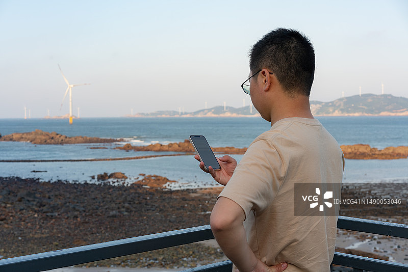 游客在日落时分用智能手机欣赏海景图片素材