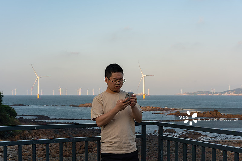游客在日落时分用智能手机欣赏海景图片素材