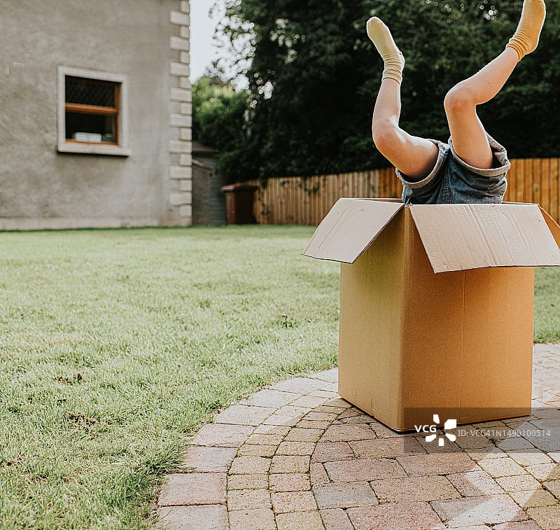 在家庭花园中，儿童的双脚从一个大型纸板箱中伸出图片素材