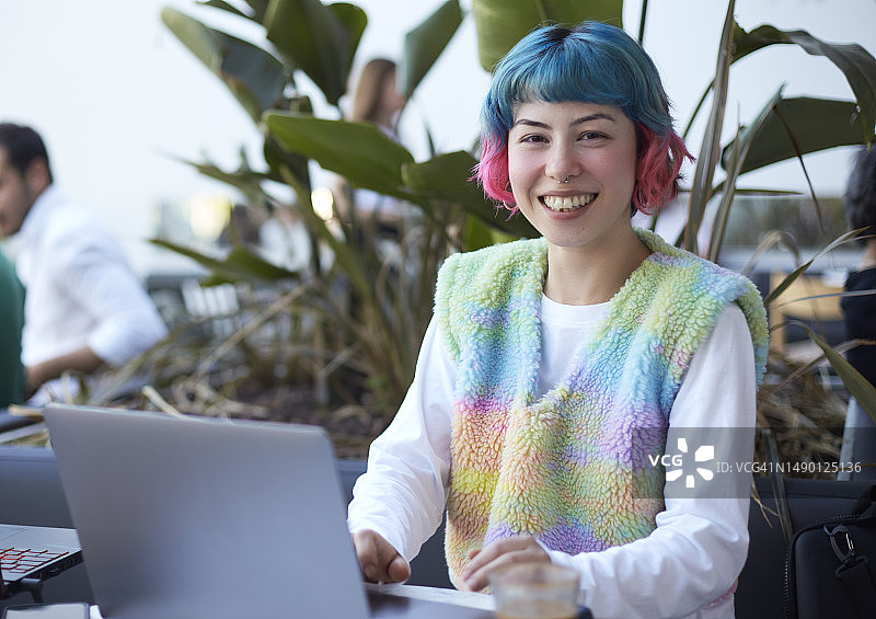 在咖啡馆用笔记本电脑工作的微笑彩色头发年轻女人图片素材