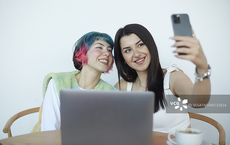 两个好朋友在电脑前工作休息时用手机自拍图片素材