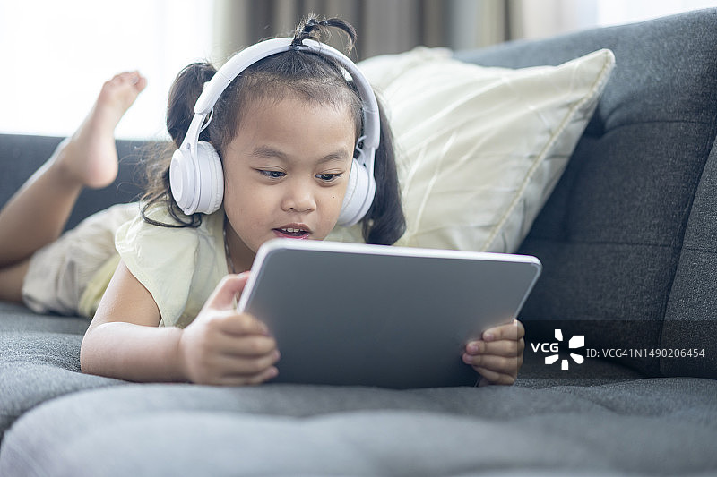 在沙发上使用数位平板和耳机的年轻女孩图片素材