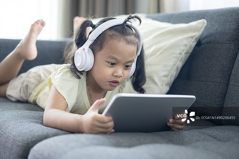 在沙发上使用数位平板和耳机的年轻女孩图片素材
