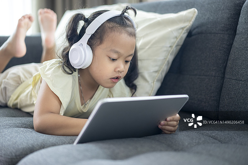 在沙发上使用数位平板和耳机的年轻女孩图片素材