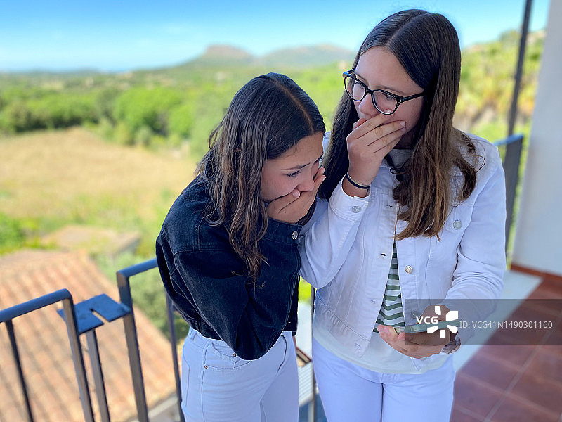 两个惊讶地用手捂着嘴看手机的年轻女孩图片素材