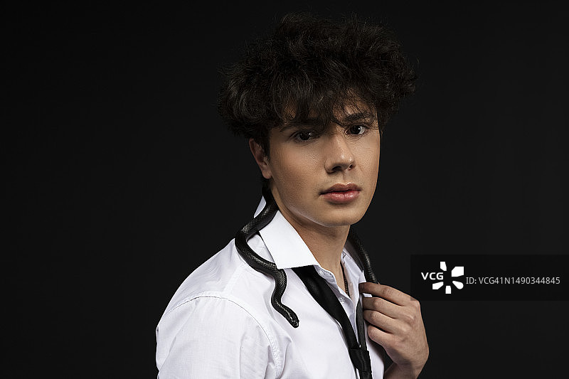 穿着白色衬衫，肩膀上爬着一条黑蛇的年轻帅哥。在黑色背景中。图片素材