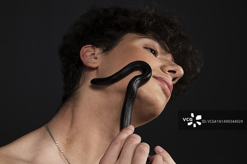 黑蛇在裸着上身的年轻男子脸上爬行图片素材