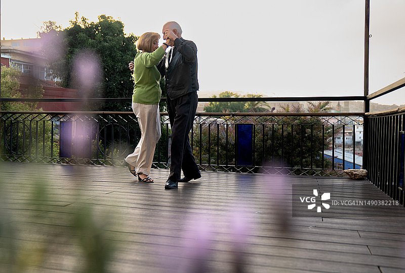 充满爱意的老年夫妇在鲜花盛开的露台上深情共舞图片素材