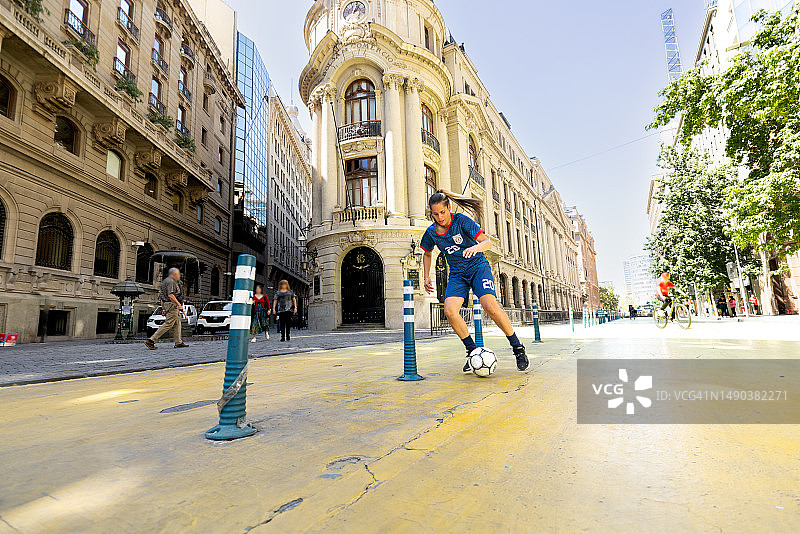 在智利圣地亚哥繁华街道上踢球的有才华的女性足球运动员的广角照片图片素材