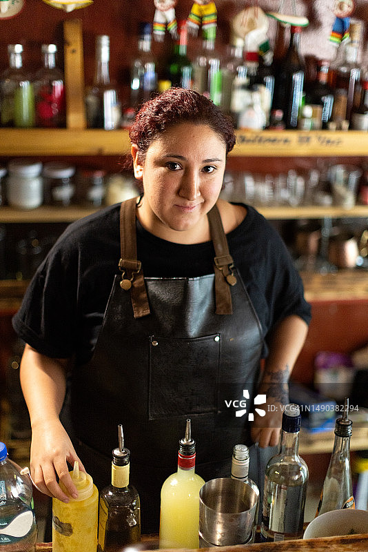 竖版照片：年轻女调酒师在吧台后工作，抬头看向镜头图片素材