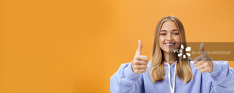 在橙色背景下竖起大拇指的微笑年轻女人肖像图片素材