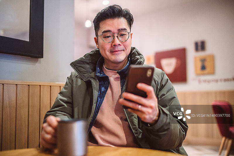 年轻的亚洲男人在咖啡馆用智能手机喝咖啡图片素材