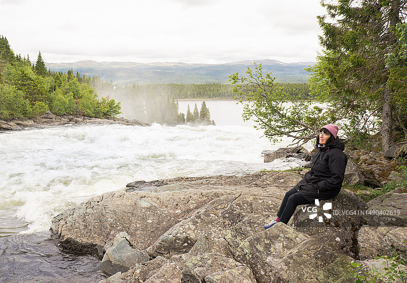 瑞典，坐在河边岩石上的女子侧视图图片素材