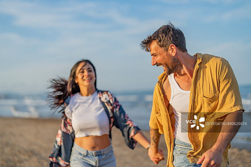 情侣在日落时牵手在沙滩上散步图片素材