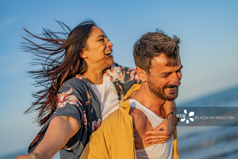 年轻情侣在海滩上享受背背乐图片素材
