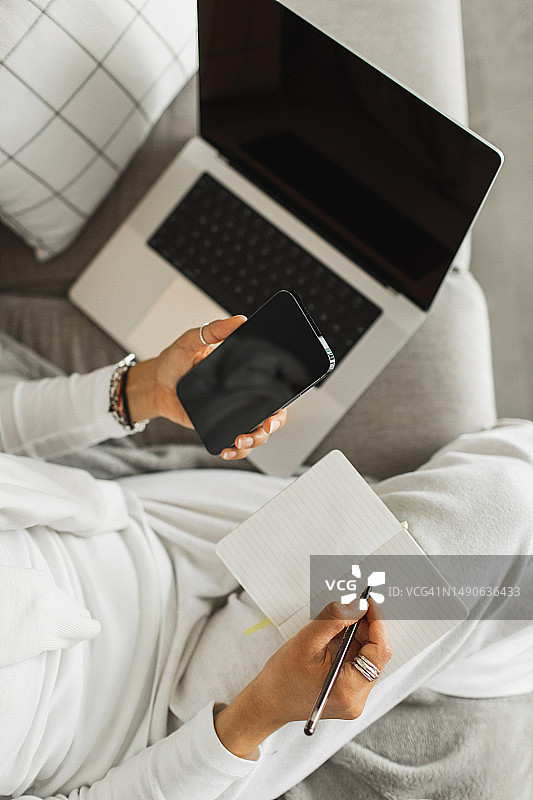 女人打电话并在笔记本上写笔记。在家工作场所，自由职业。在线咨询图片素材