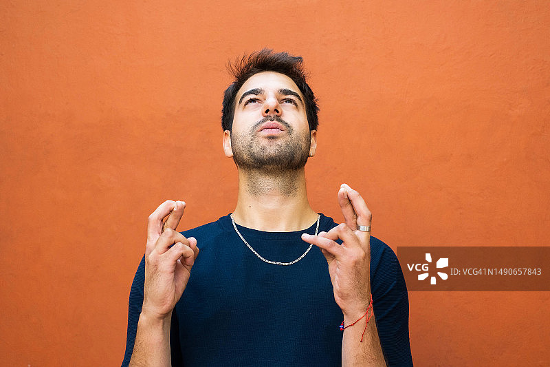 拉丁裔男子抬头并交叉手指，充满希望地许愿图片素材