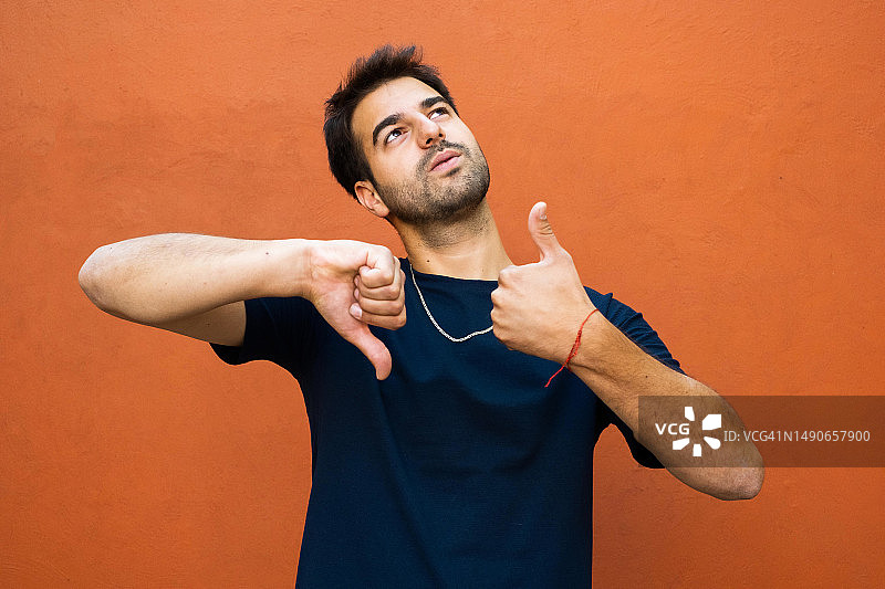 向上看并竖起大拇指和倒竖大拇指的拉丁裔男人图片素材