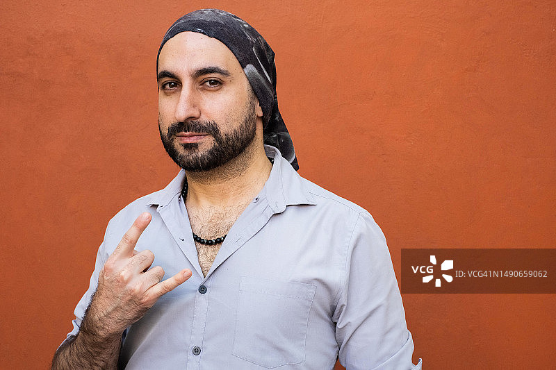 戴着头巾、看着镜头并做出重金属摇滚手势的中东裔拉丁男人图片素材