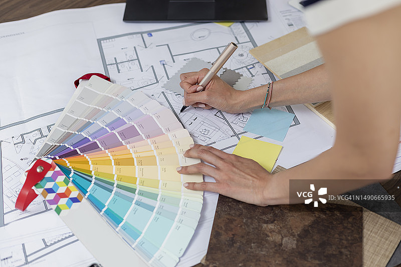 建筑师在项目图纸上做笔记的手部特写，附带样品和潘通色卡图片素材
