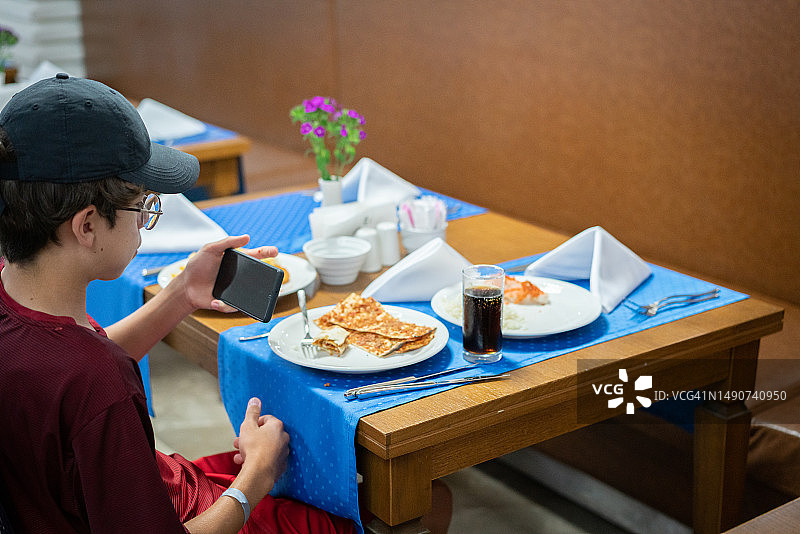 男孩在餐厅用智能手机拍摄食物图片素材