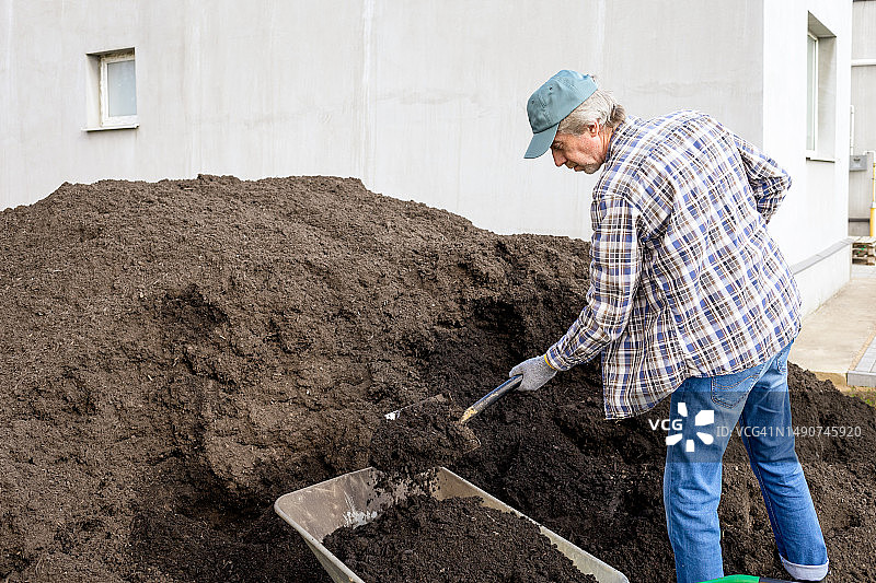 一位50岁的男性农民用铲子挖一堆有机肥料图片素材