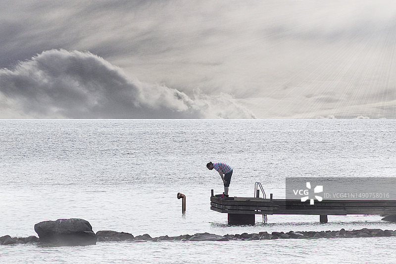 男人站在瑞典海边的码头上，背景是天空图片素材