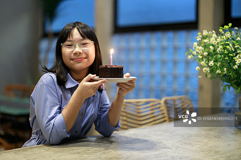 一位快乐的亚洲女孩拿着点燃蜡烛的生日蛋糕，对着镜头温暖地笑着图片素材