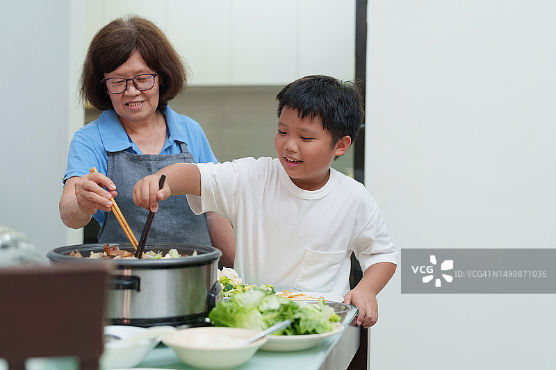 快乐的孙子和奶奶在家愉快地享用蒸汽火锅图片素材