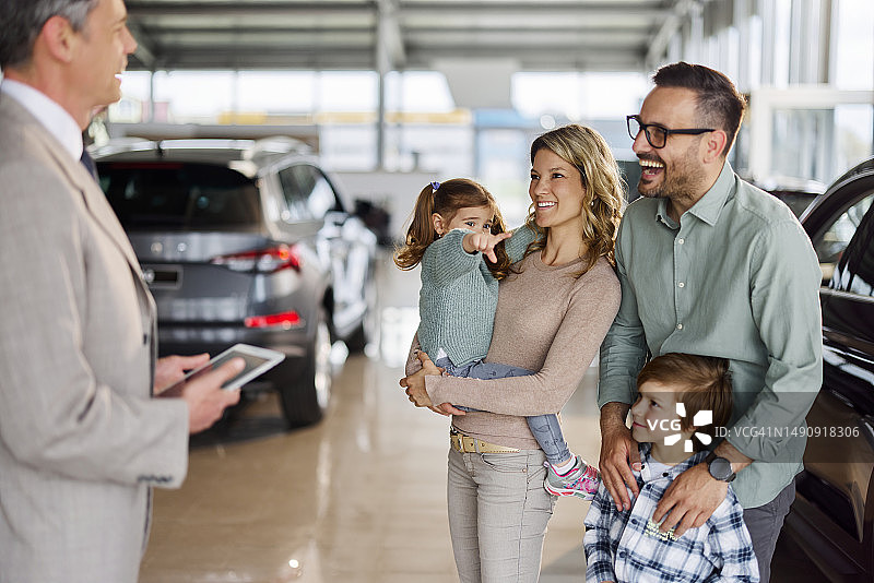 幸福的年轻家庭在展厅与汽车销售交谈图片素材