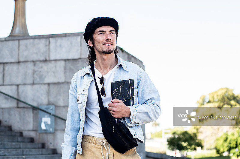 在街上拿着笔记本沉思的年轻男学生图片素材