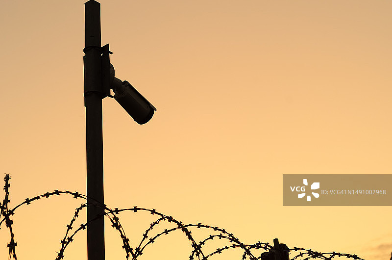 日落时，杆子上安全摄像头的轮廓，用带刺铁丝网观察保护区的周边，罗马尼亚文字空间图片素材