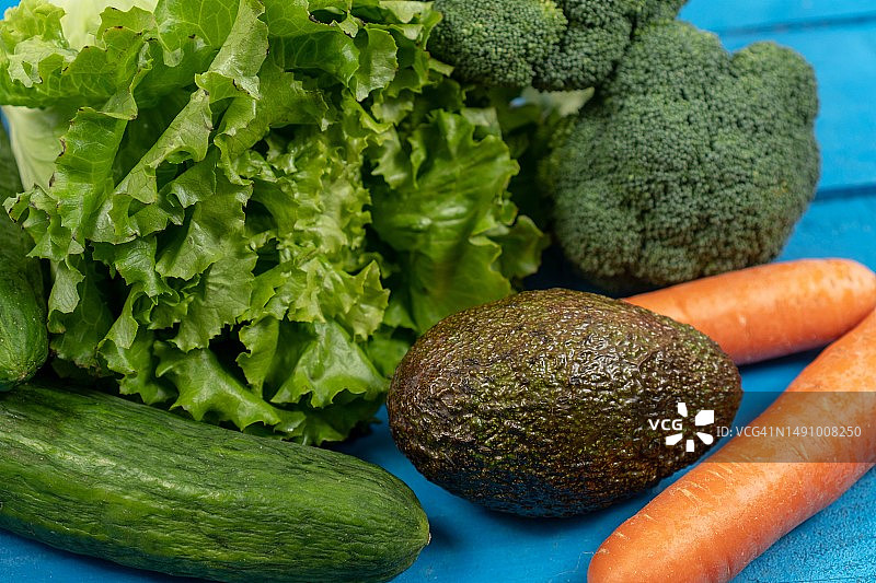 蓝色木板上的新鲜胡萝卜、鳄梨、西兰花、生菜和黄瓜，罗马尼亚图片素材