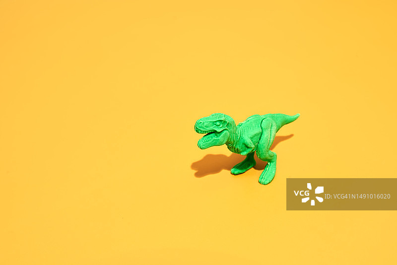 黄色背景上的绿色塑料霸王龙图片素材