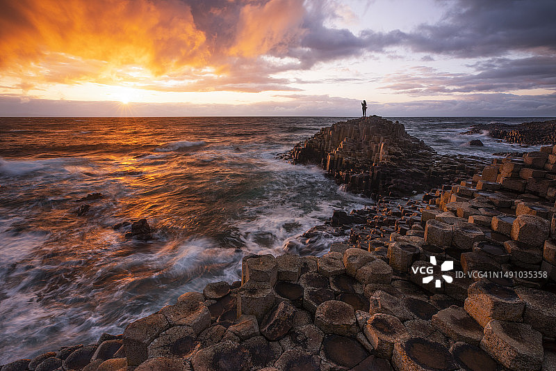 女孩欣赏巨人之路美丽的日落，位于欧洲爱尔兰图片素材