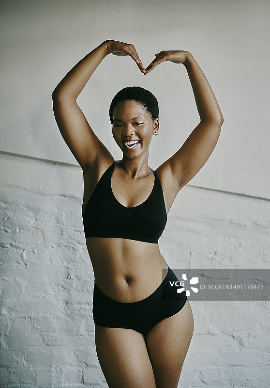 爱上自己。年轻有魅力的黑人女性站着，笑着，用手在头顶比心图片素材
