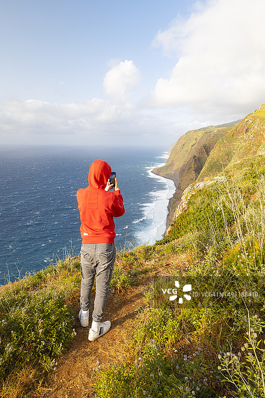 在葡萄牙马德拉岛，男孩用智能手机拍摄帕尔戈角灯塔附近的悬崖图片素材