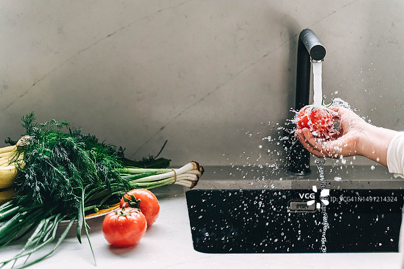 在现代厨房里，人在黑色水龙头下洗菜图片素材