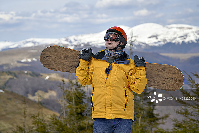 戴滑雪头盔和面罩，在山上扛着滑雪板的男子图片素材