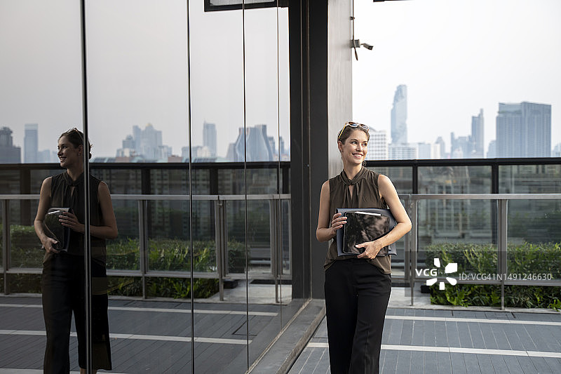 在现代办公楼里拿着平板电脑的自信商务女性图片素材