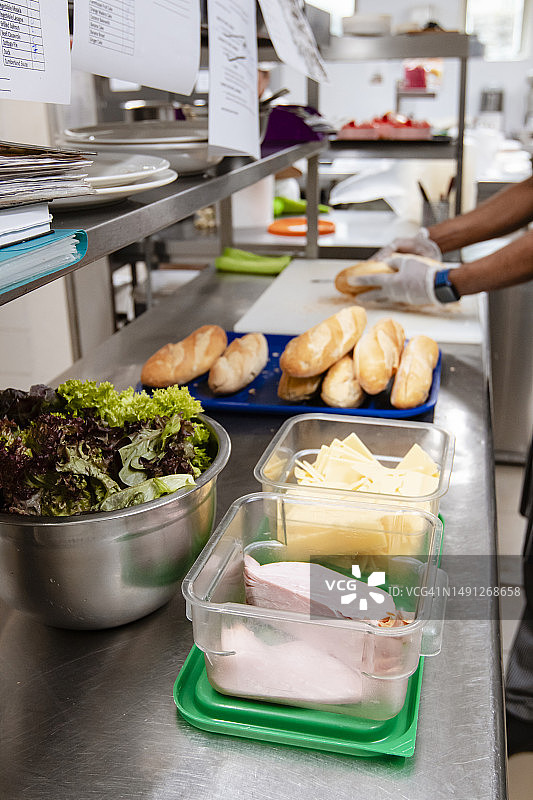专业厨房备餐区，容器中的食材，厨师在背景中切法棍图片素材